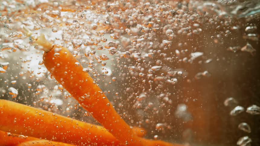 Carrots are cooking in a pot of water as bubbles rise to the surface