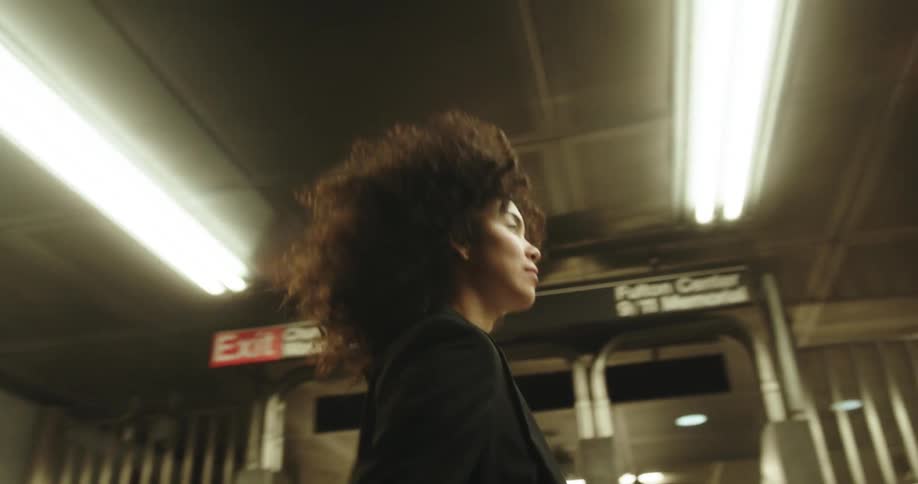 A woman walking through a subway station with a slight smirk on her face