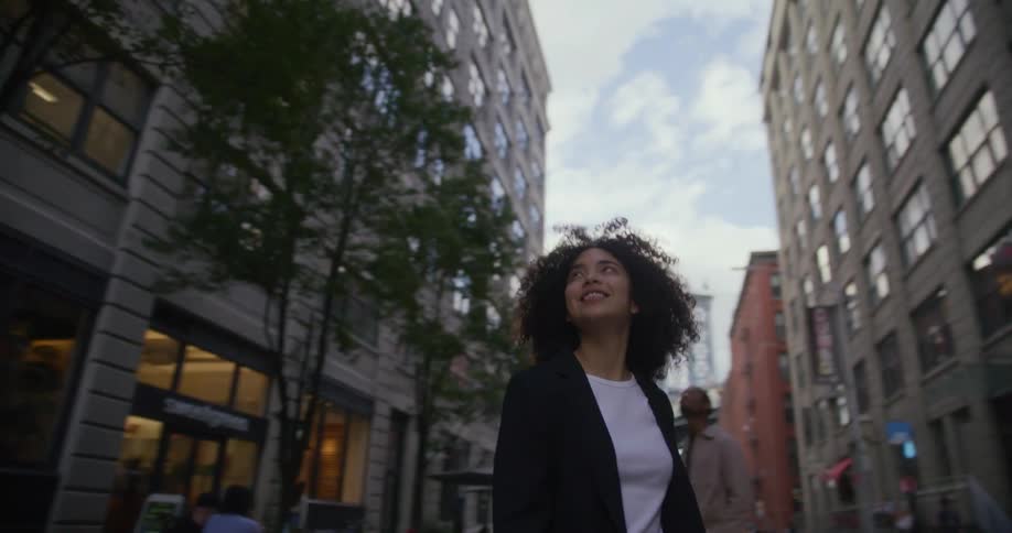 A man and a woman stand in a city street surrounded by several buildings they look at in awe