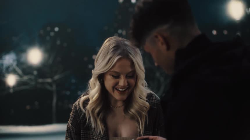 A man and woman sitting on a bench outdoors as the man proposes to the woman and she says yes