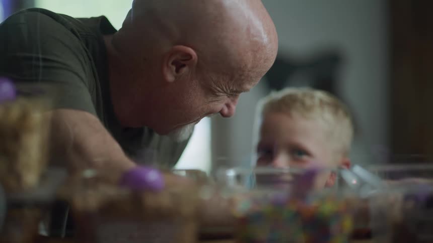 An older bald man smiles as he is talking with a young boy
