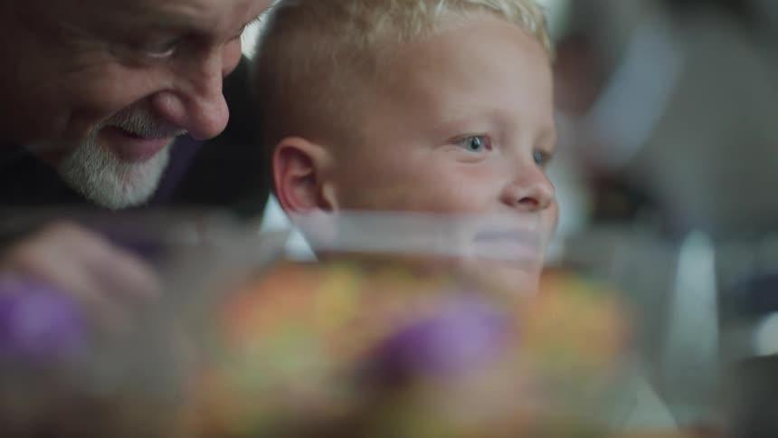 A boy looking thinking before his father comes over and the boy points and smiles