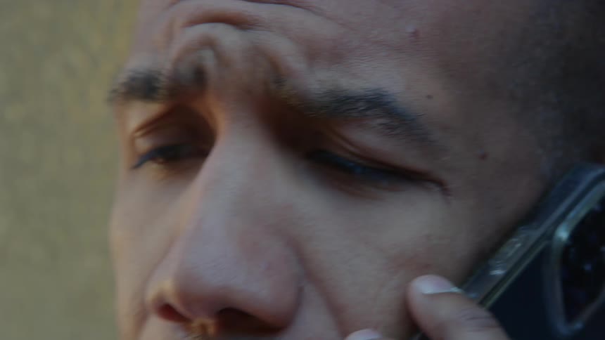 A close up of a mans face while he talks on his cellphone