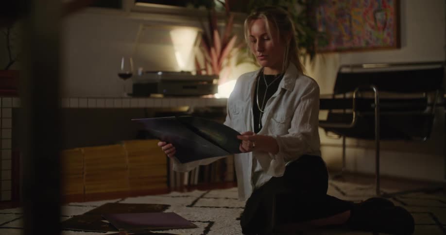 A woman is sitting on a rug on the floor looking at a vinyl record album