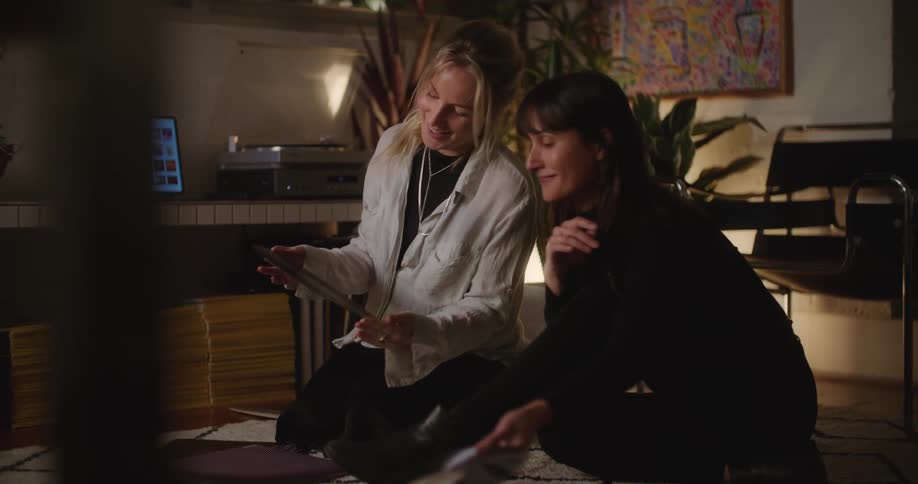 Two women sitting on the floor looking at record albums smiling and laughing
