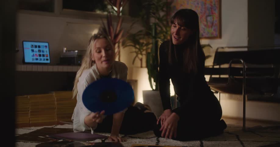 Two women sit on the floor while looking through a stack of records
