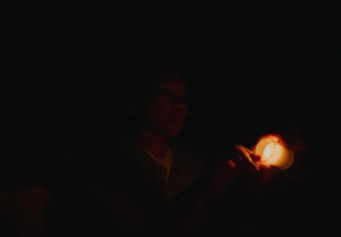 Mother sitting at dining table with son who is standing lighting candles with a box of matches in the dark