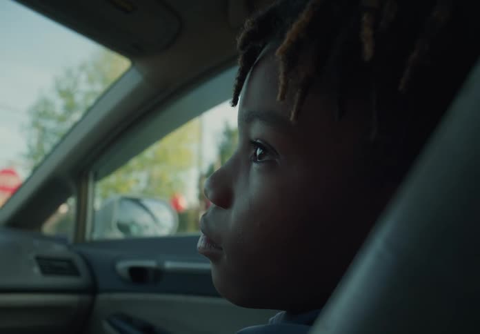 A young boy is sitting in the passenger seat of an automobile as it travels through a neighborhood