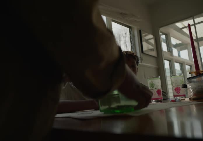 Two young boys sit at a table and an adult brings them something in a container