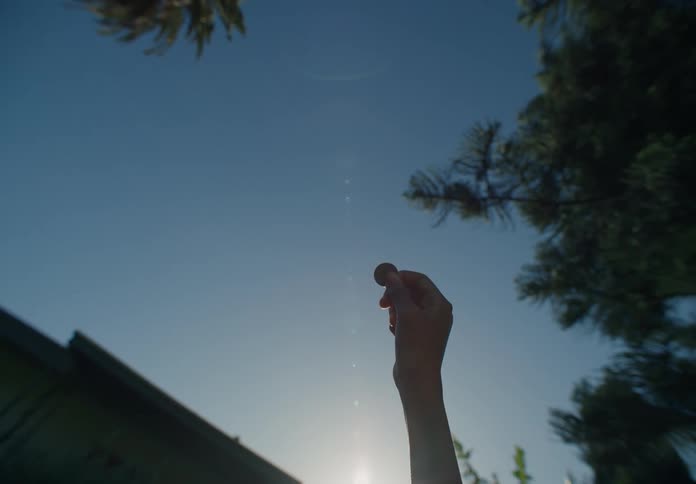 Outdoors near house person holds a silver coin up against bright sky