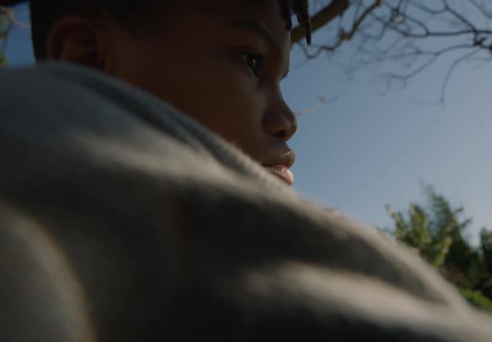 Youth frowns and stares while swinging on backyard swing as he thinks