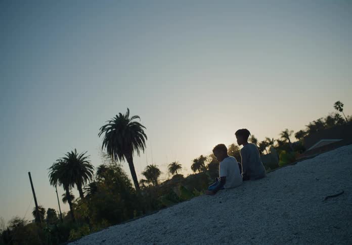 A time lapse shows two young brothers sitting together outside as the sun sets