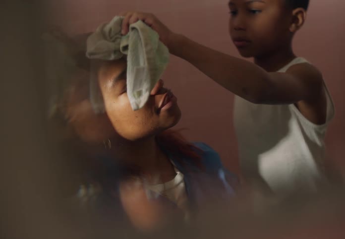 A boy cares for his ailing mother who has a fever by tapping the sweat of her forehead with a cloth