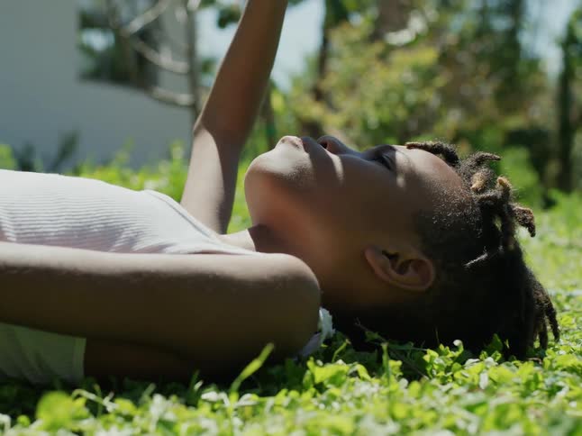 Boy with dreadlocks and white undershirt lies on green lawn in the yard