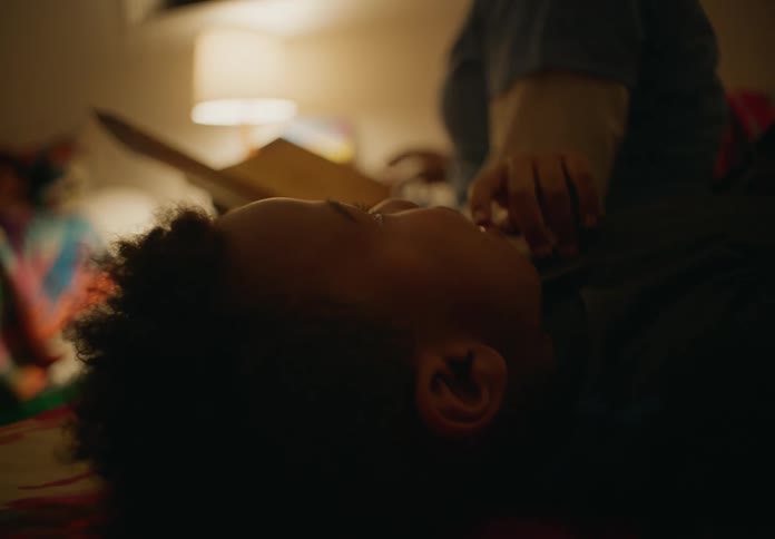 A young bpys lays on his back while another person nearby holds a book