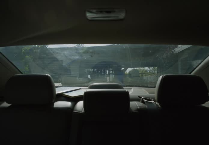 Woman walks out of the house tying her hair on a ponytail seen from the interior of a vehicle