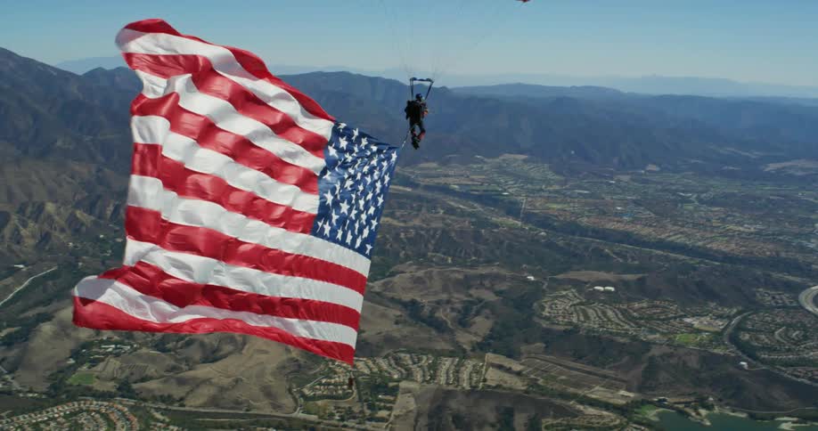 An aerial view of a person parachuting to the ground with the united states flag waving from their back