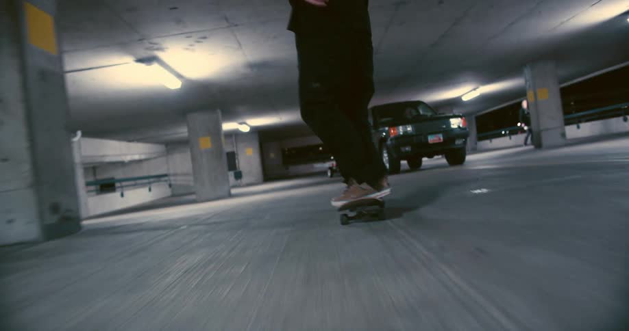 Men in black shirts and pants skateboard in parking garage at night