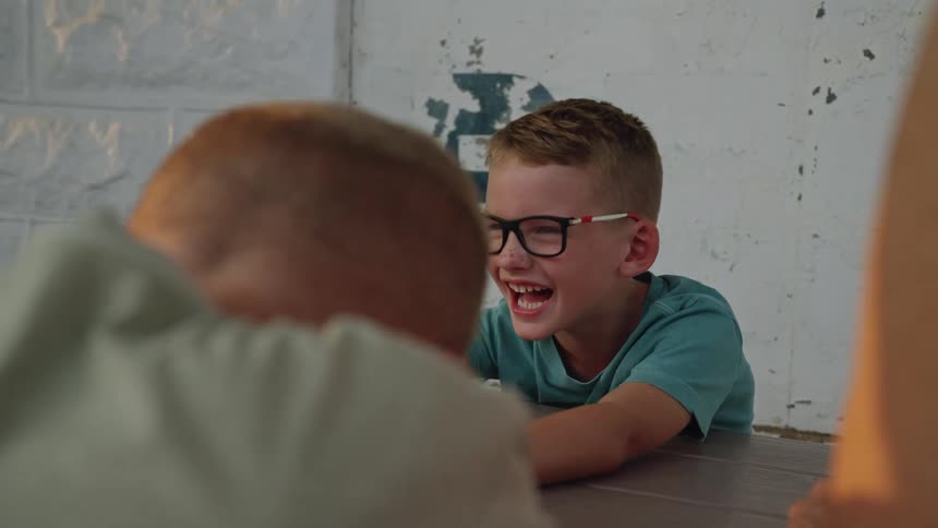 Three boys are sitting at a table laughing hysterically
