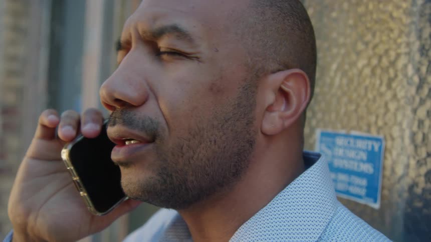 A man is standing near a building talking on his cell phone