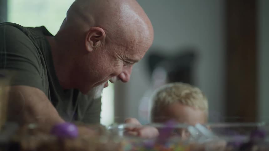 A bald man turns to smile at a young child seated near him indoors