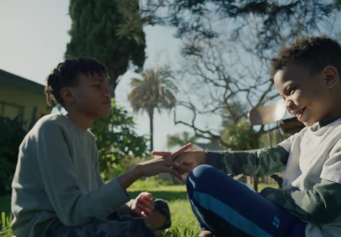 Two young brothers are sitting on the grass outside their house and playing a game