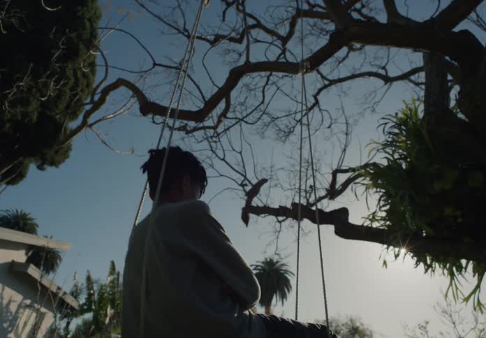 Boy with dreadlocks and gray sweater on the swing in the garden