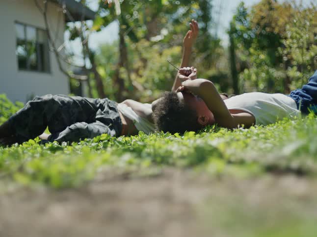 Two boys laying on their backs in the grass in their back yard looking up at the sky