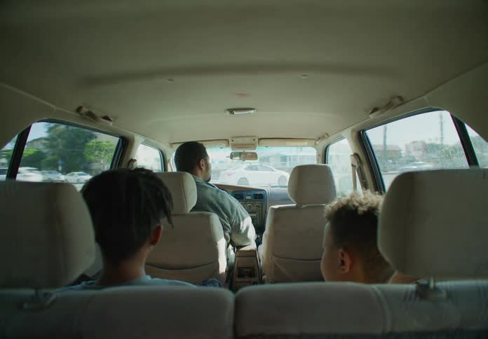 Father drives a car through the city at daytime talking with the children sitting in the back