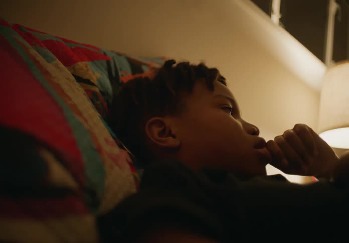 A boy leans back on a colorful pillow near a lamp