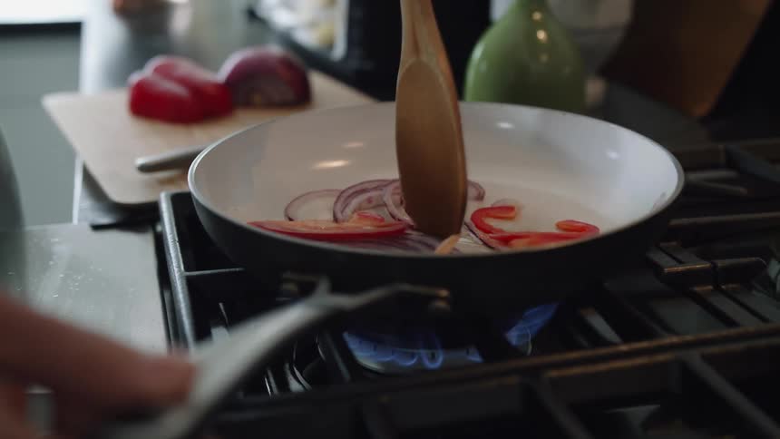 A person is sauteing fresh vegetables in a skillet on a gas stovetop