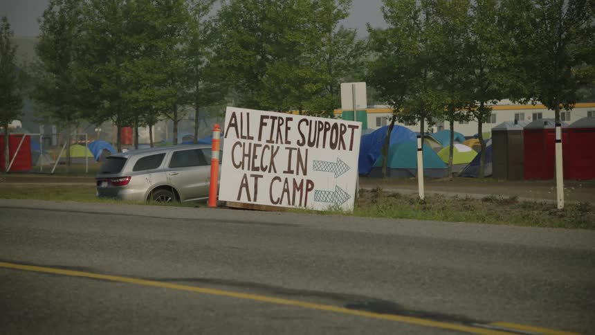 Hand made sign at the side of the road next to a camp full of tents in the city