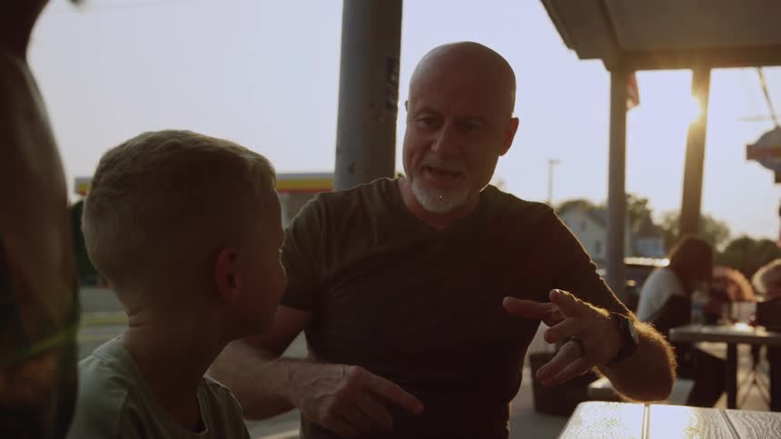 Father and son talk while sitting on the table of an outdoors restaurant at evening