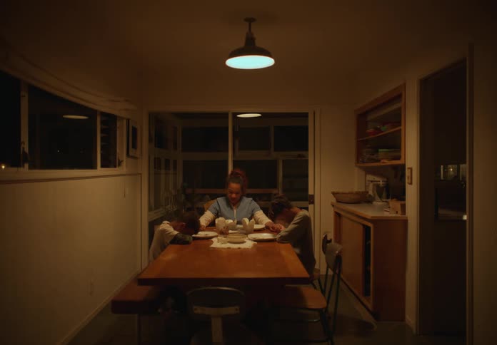 A woman and two boys sit at a table indoors and hold hands to say grace