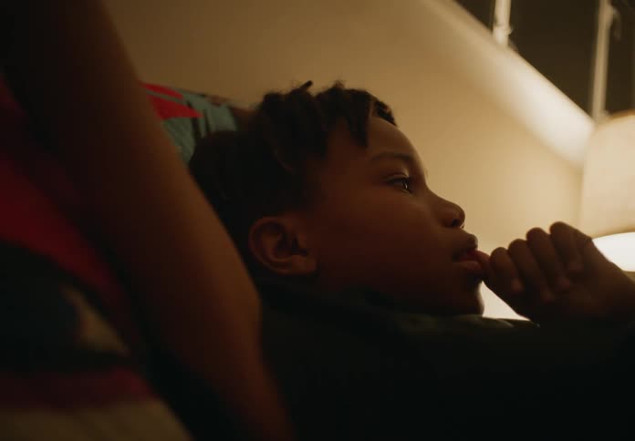Youth leans against pillow in room lit by lamp and thinks