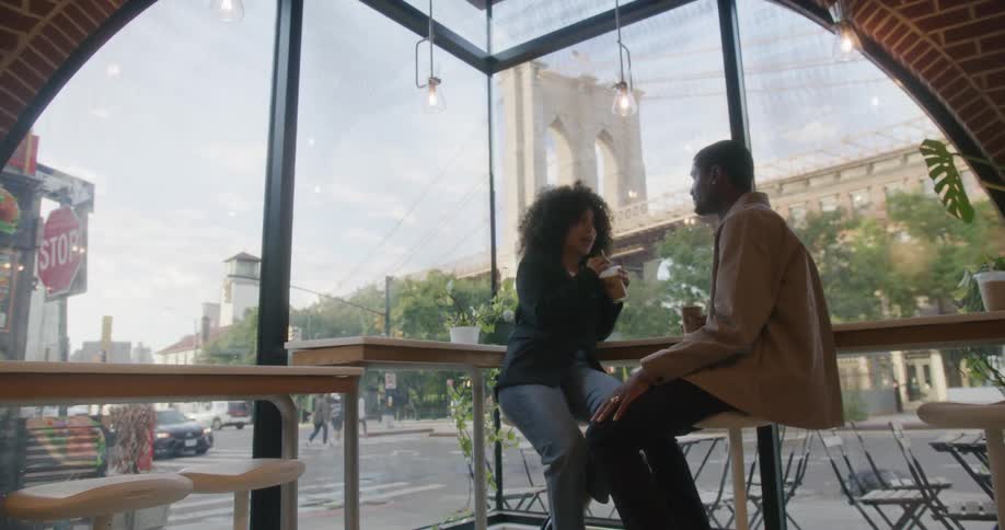 Young couple sitting at bar near window in coffee shop each drinking an iced coffee