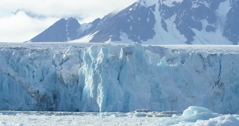 A large ice cliff is before a mountain