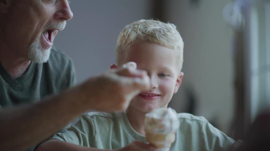 A grandfather takes a spoonful of ice cream from his grandsons ice cream cone