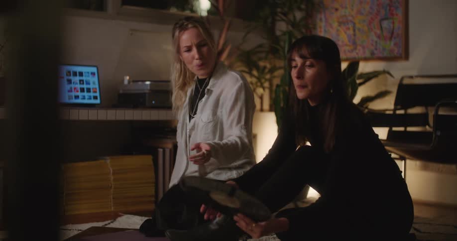 Two women go through vinyl records while sitting on the floor