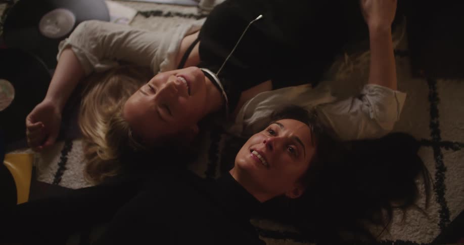 Two friends lie on their backs in opposite directions and talks with their heads close together