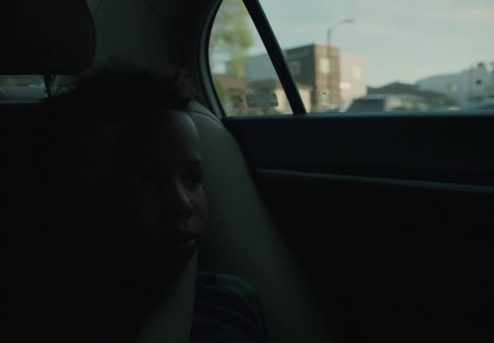 A young boy is sitting in the back seat of an automobile as it travels through a neighborhood