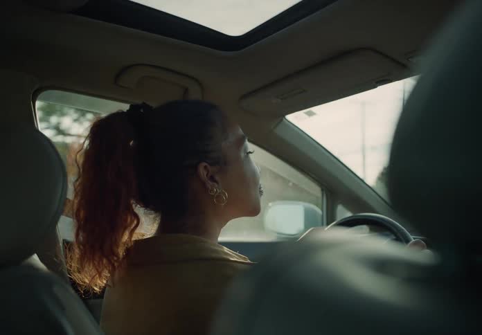 Woman with a ponytail looks around while driving a car through the city at morning