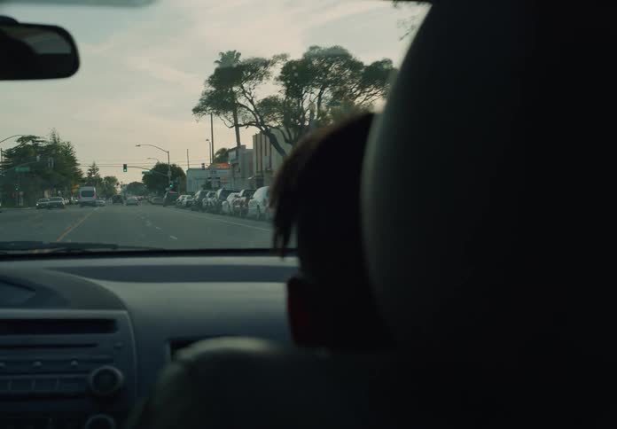 A close up of the back of a childs head riding in a car driving down the road approaching an intersection