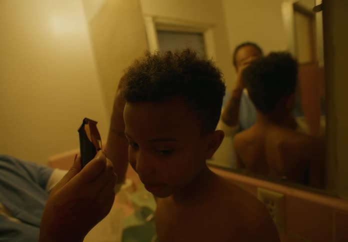 Mother using clippers to trim young sons hair in the bathroom while he sits on the bathroom sink