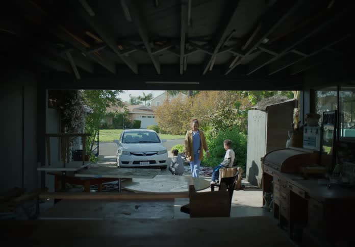 A mother and her sons are walking around and kneeling in the driveway outside their house