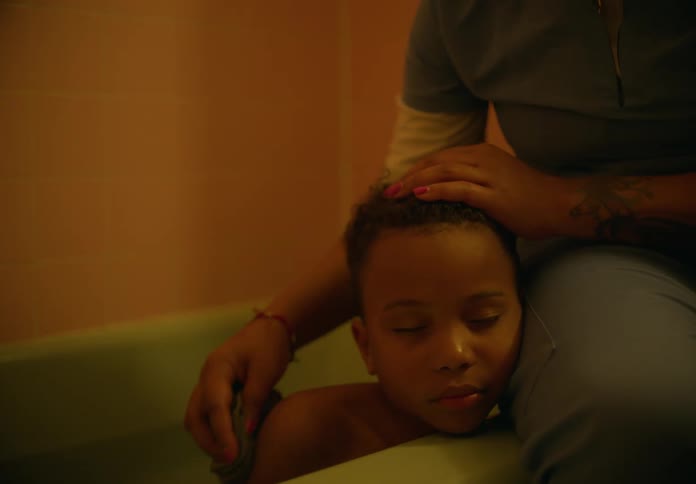 Mother with green shirt and pants rubs sons back and head sitting in bathtub