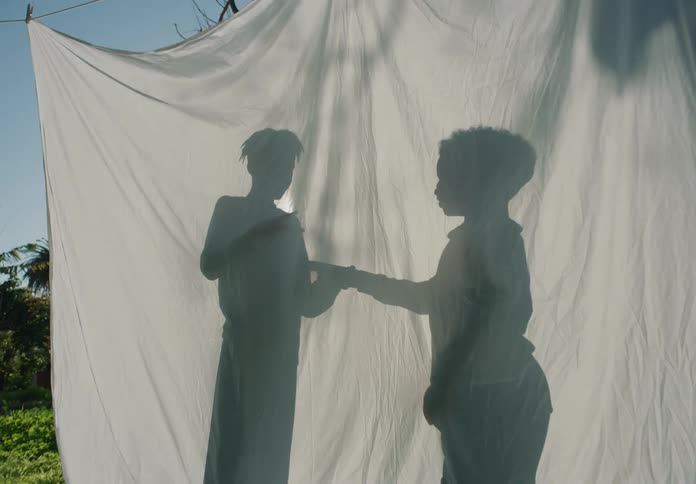 Shadow of two boys playing rock paper scissors behind a white sheet outdoors