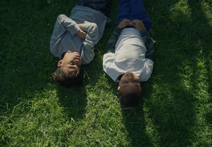 Tween brothers lying on their backs in the grass talking and bonding during the day