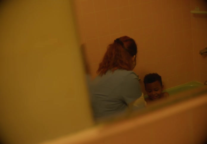 A young boy sits in the bathtub while happily talking to his caretaker