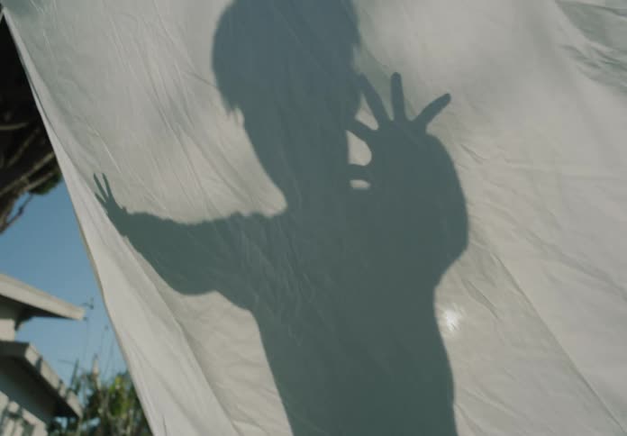 Young boy plays projecting his shadow on a white bed sheet hanging in the backyard